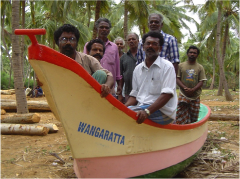 A group of 8 people sit in a fishing boat on dry land. The boat has "Wangaratta" written on it.