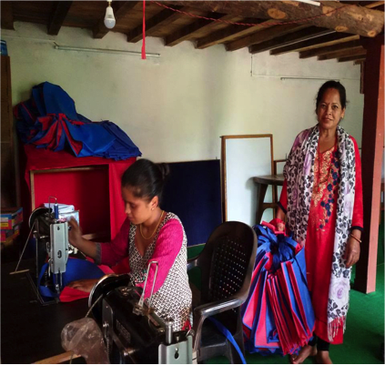 An image of two women inside a room. One is sitting at a sewing machine and one stands behind her holding the fabric.